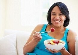Woman Sitting On Sofa Eating Bowl Of Fresh Fruit At Home Looking Happy